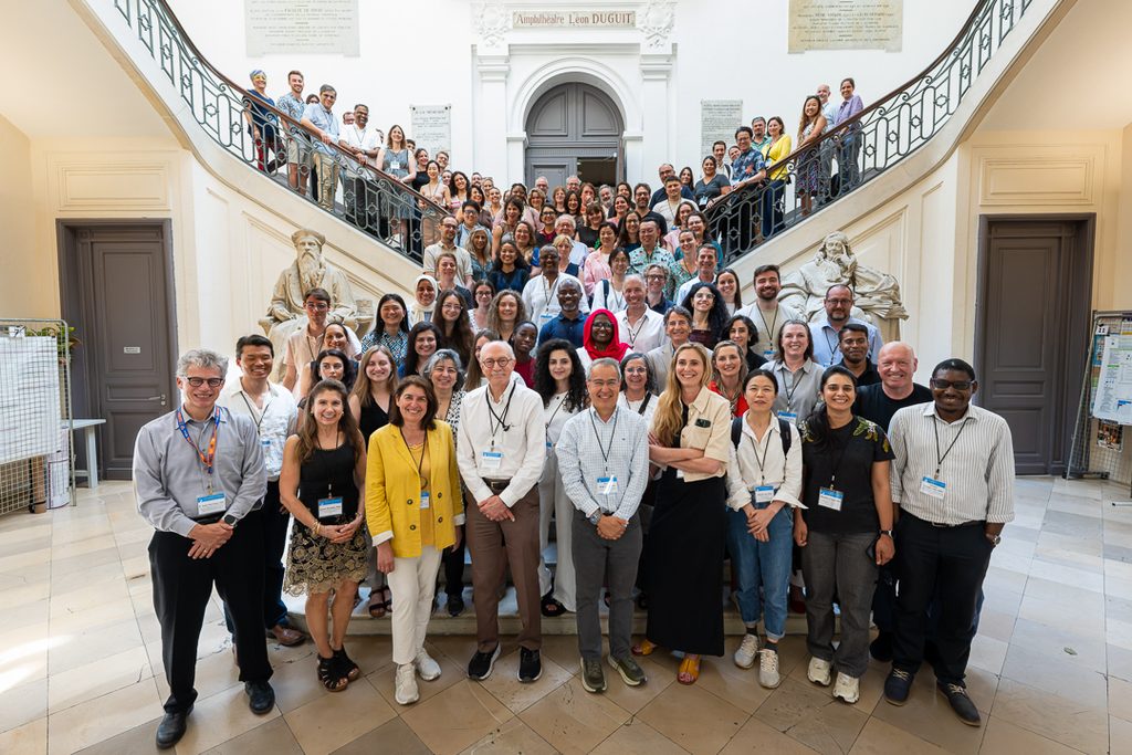Attendees of the Global Exposome Symposium looking at the camera with a background of a large grand staircase